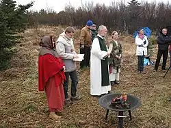 Eight people, all white, stand on heathland. Some of them are dressed in historical clothing akin to that worn in the medieval period.