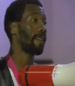 Black South African man in a vest, holding a megaphone.