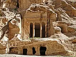 A colonnades classically styled temple carved out of a beige-colored rock cliff face.