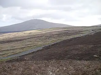 Snaefell mountain in distant haze rising above rough low vegetation animal grazing land against a pale cloudy sky