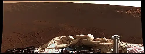 Figure 2. View from Opportunitys Pancam on sol 1. The stainless steel column in the foreground is part of the rover's communications system. The fabrics in the foreground are deflated airbags and parts of the lander system (they are not part of the rover). In the near-middle-ground are soils compacted by the lander's airbags. The rest of the image shows red soils covered in grey spherules and the rim of Eagle Crater. A lighter rocky outcrop of the crater's rim is in the right background. Image taken on Sol 1 (2004-01-24).