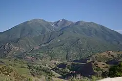 a river is in the center of the picture, with a canyon wall and mountains visible on the right side. To the left of the river is a black streak, remains of a rail line. To the right of the river is an abandoned road, with a new road and rail line in cuts along the canyon wall.