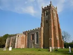 A bbuttressed rick tower with battlemented parapet, and the body of the flint church beyond
