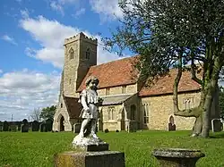 A stone church with red tiled roofs seen from an angle, the battlemented tower being on the left.