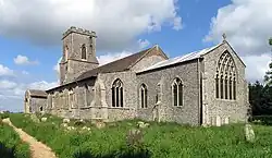A stone church seen from the southeast, showing the chancel, beyond which is a taller nave with a south aisle and porch, and a battlemented tower