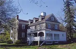 A large stone house with many dormers, windows, and a white porch, surrounded by trees