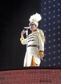 Swift singing onto a mic, dressed as a drum majorette