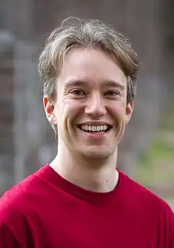 Head shot of Scott wearing a red T-shirt, smiling and standing outside