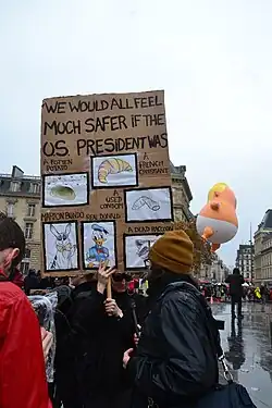 crowd in the rain, poster of Trump face, Baby Trump balloon, around statue of Marianne