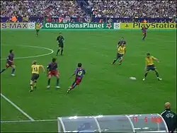 A coloured action photograph of a football match in progress. There are a group of men, four of which wearing yellow shirts and black shorts. Five are wearing red and blue striped shirts.