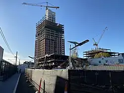 A high-rise building under construction with tall crane along side a light rail station platform