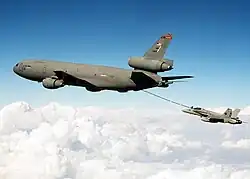 A jet aircraft refuels from a gray three-engine tanker via a long boom located under the tanker's aft fuselage.