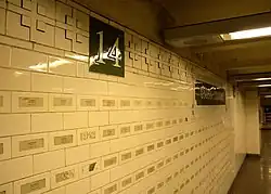 A wall of white tiles on the station's mezzanine. Stickers with the names of 9/11 victims are placed on the tiles.