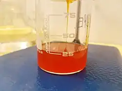A beaker being filled with a viscous reddish orange liquid