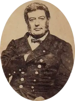 Photographic portrait of a dark-haired man with sideburns, dressed in a double-breasted military tunic with his right hand tucked under the lapel of his jacket