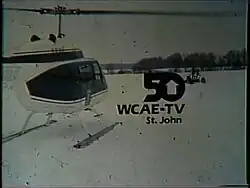 An ID slide showing a white helicopter landed in a snowy field. A black "50", with the counter of the zero being an upward-pointing arrow, is slightly off center. Below it is the text "WCAE-TV, St. John".