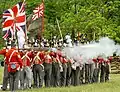 Re-enactors (in UK uniforms) fire muskets toward the "Americans" in annual commemorations