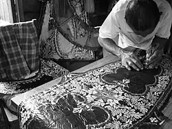 A wau-maker in his workshop. Design details in his wau are made by cutting various layers of coloured paper. The cutting is done spontaneously.