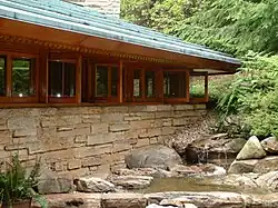 The facade of Kentuck Knob, which is made of stone, wood, and glass. There is a water feature outside the house.