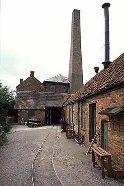 Several red brick buildings and a chimney, with parallel rail tracks in the foreground