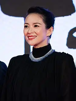 A short-haired woman wearing a black outfit along and a white and blue necklace poses for the camera